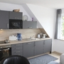 Moderne Einbauküche mit grauen Schränken und Esstisch in heller Ferienwohnung.