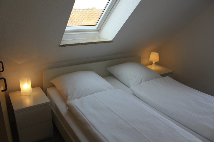 Doppelbett in gemütlichem Schlafzimmer mit Dachfenster und Nachttischen.