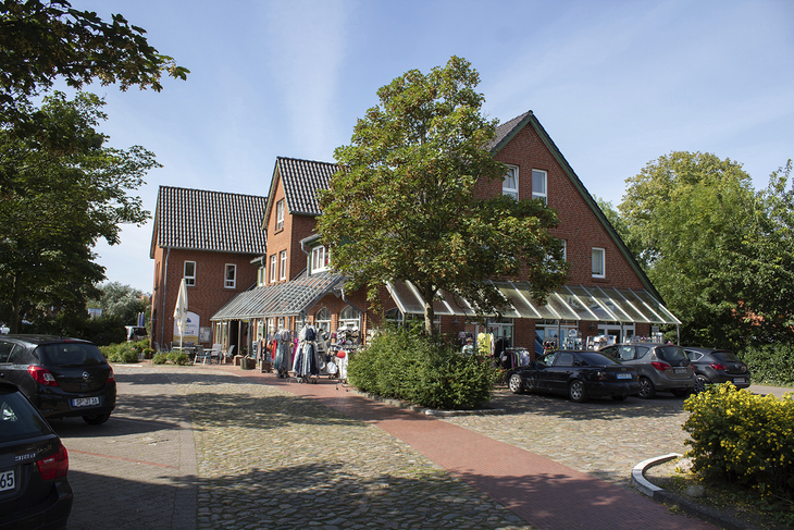 Feriendomizil mit Backsteinfassade, Bäumen und geparkten Autos bei Sonnenschein.