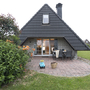 Haus mit schwarzem Dach, Terrasse, Stuhl und Spielzeugauto im Garten.