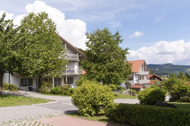 Ferienwohnungen in einer grünen, hügeligen Landschaft mit blauem Himmel und Wolken.