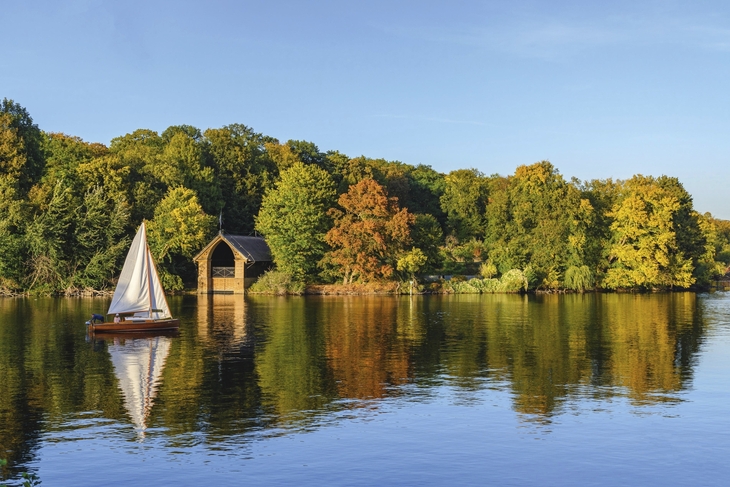 Segelboot auf dem Wannsee vor buntem Herbstwald und Bootshaus.