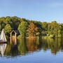Segelboot auf dem Wannsee vor buntem Herbstwald und Bootshaus.