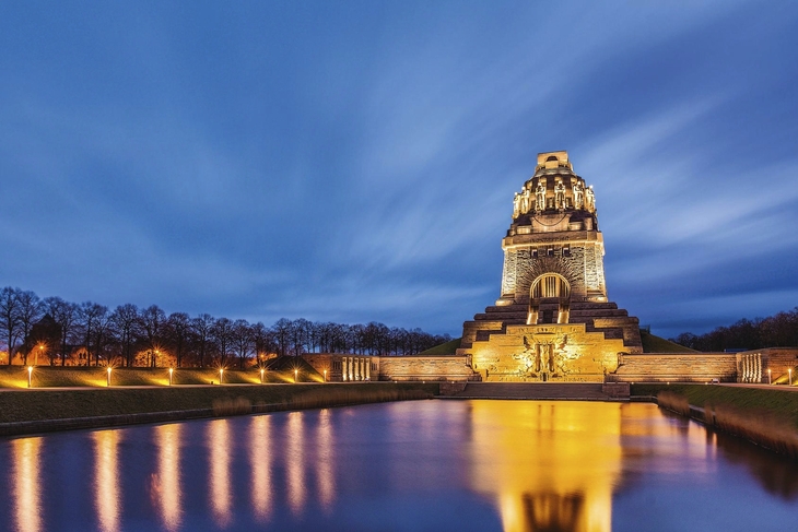 Völkerschlachtdenkmal in Leipzig bei Abenddämmerung, angestrahlt und reflektiert im Wasser.