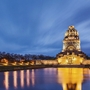 Völkerschlachtdenkmal in Leipzig bei Abenddämmerung, angestrahlt und reflektiert im Wasser.