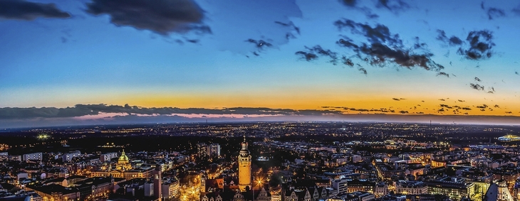 Stadtpanorama von Leipzig bei Sonnenuntergang mit Wolken und beleuchteten Gebäuden.