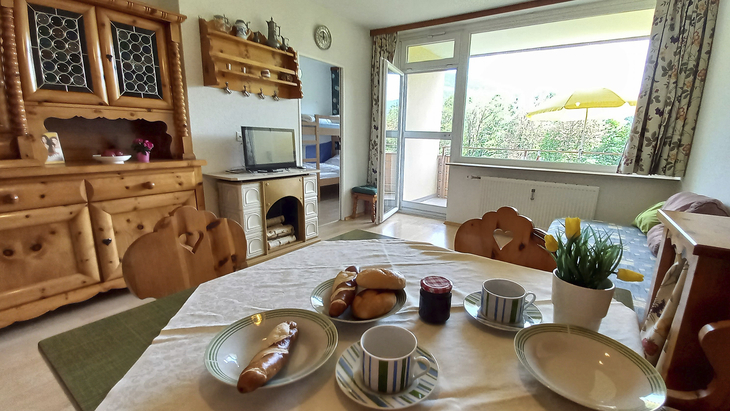 Essbereich in Appartement mit gedecktem Tisch und Ausblick auf Balkon und Garten.