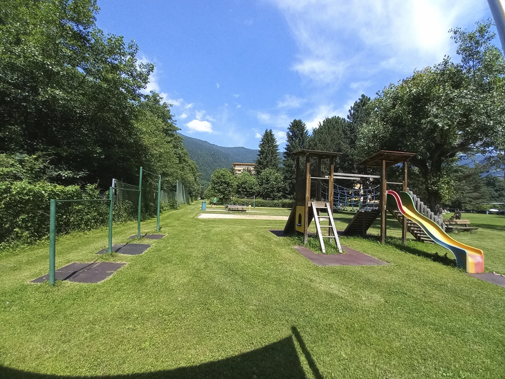 Spielplatz mit Rutsche und Klettergerüst in grüner Umgebung an einem sonnigen Tag.