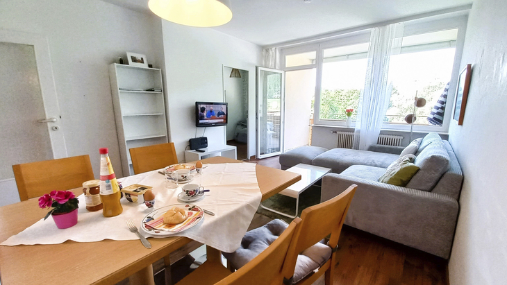 Wohnzimmer einer modernen Ferienwohnung mit Esstisch und gemütlichem Sofa.