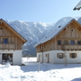 Zwei Chalets im Schnee vor Bergkulisse bei klarem Himmel.