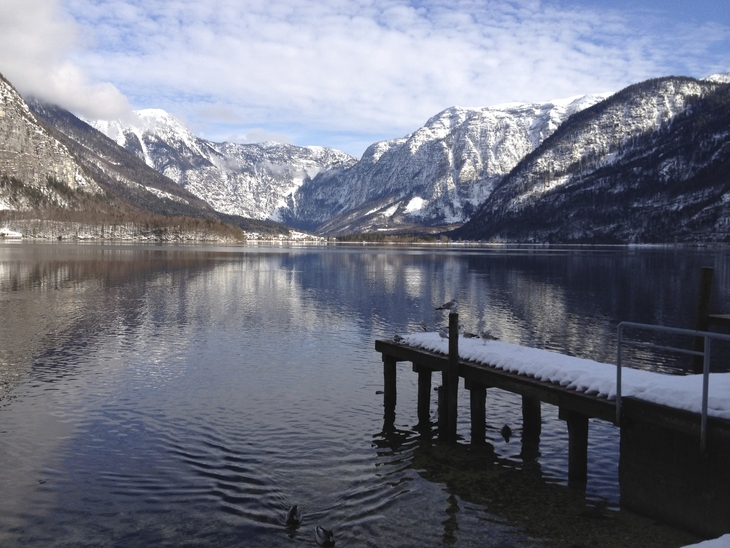 Landschaft mit See, schneebedeckten Bergen und einem Steg im Vordergrund.