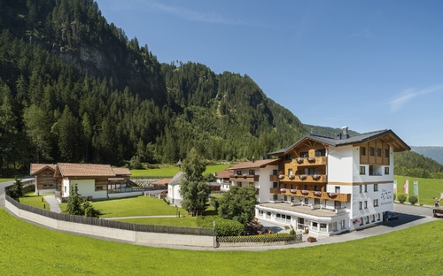 Hotel in Berglandschaft mit grünem Rasen und bewaldeten Hügeln im Sommer.