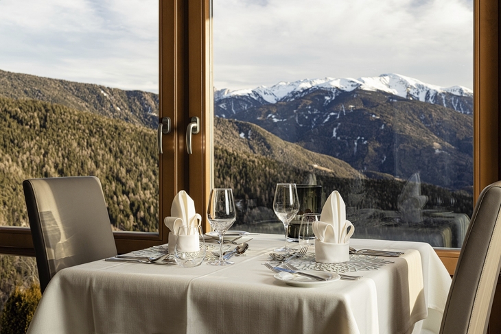 Gedeckter Tisch mit Bergblick durch großes Fenster.