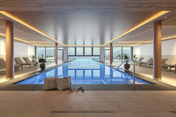 Innenpool in einem Wellnessbereich mit Liegestühlen und großen Fenstern im Hintergrund.