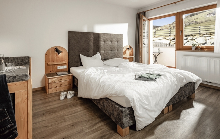 Helles Doppelzimmer mit Bett, Holzmöbeln und Blick auf die Wiesen.