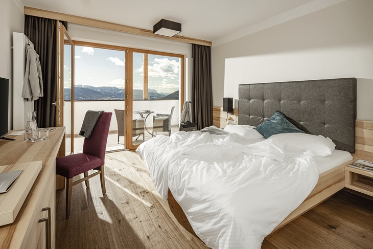 Doppelzimmer mit Bett und Balkonausblick auf Berge.