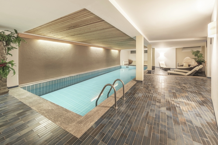 Innenansicht eines modernen, beleuchteten Schwimmbads mit Liegestühlen.