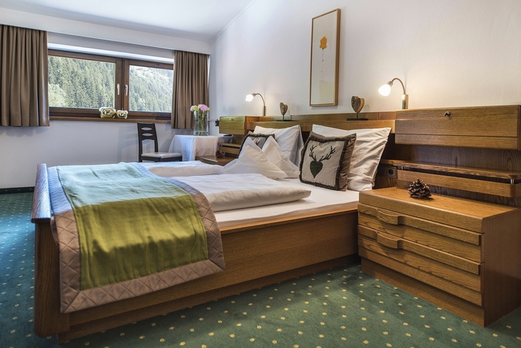 Gemütliches Schlafzimmer mit Doppelbett, Holzmöbeln und Fensteraussicht auf Berge.