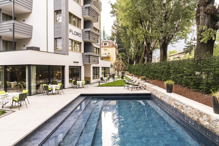Außenbereich des Hotels Flora mit Pool und Liegen im Garten.