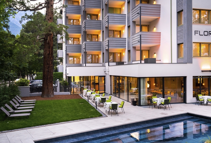 Außenfassade eines Hotels am Abend mit beleuchteten Balkonen und Terrasse.
