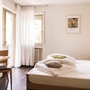 Doppelzimmer mit Bett, Tisch und Stuhl, helle Vorhänge und Bild an der Wand.