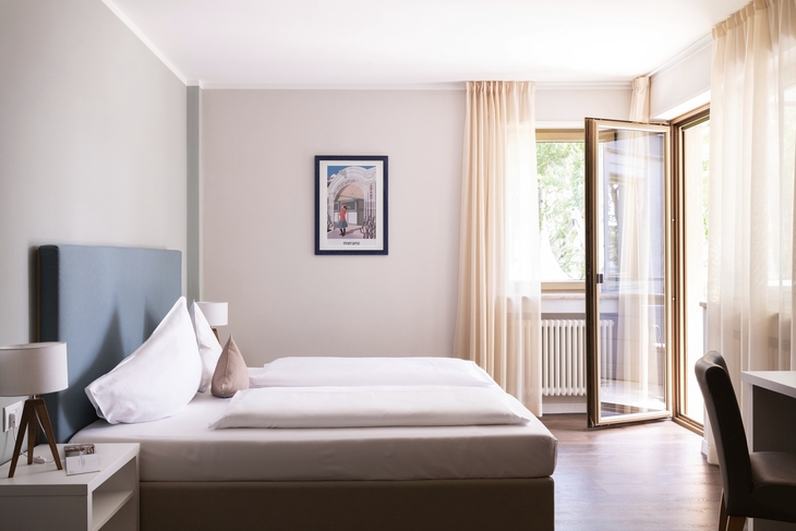 Helles Hotelzimmer mit Doppelbett und offenem Fenster.