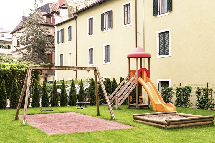 Spielplatz mit Schaukel und Rutsche vor einem Hotelgebäude