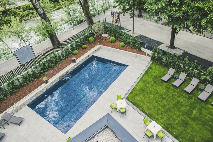 Ausblick auf Pool und Garten des Hotel Flora in Meran mit Liegestühlen und Bäumen.