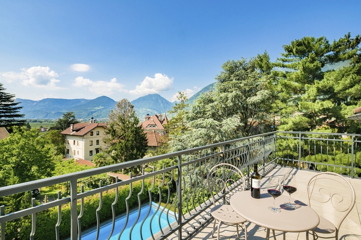 Terrasse mit Blick auf Pool, Garten und Berge bei klarem Himmel.