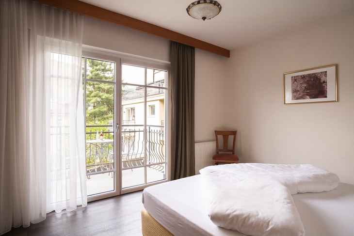 Doppelzimmer mit Balkon und großen Fenstern, geschmackvoll eingerichtet.