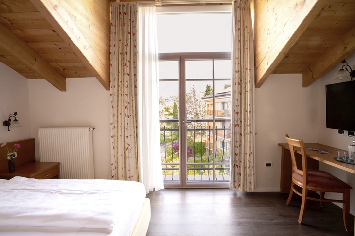 Helles Hotelzimmer mit Holzmöbeln und Balkonblick auf die Umgebung.