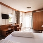 Helles Hotel-Doppelzimmer mit Doppelbett, Schreibtisch und großem Fenster.