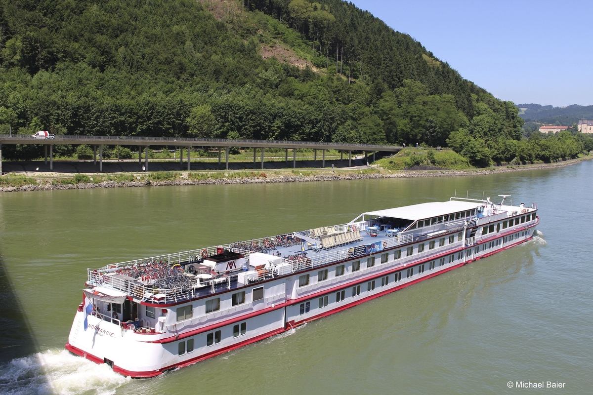 Kreuzfahrtschiff auf einem Fluss, umgeben von bewaldeten Hügeln.