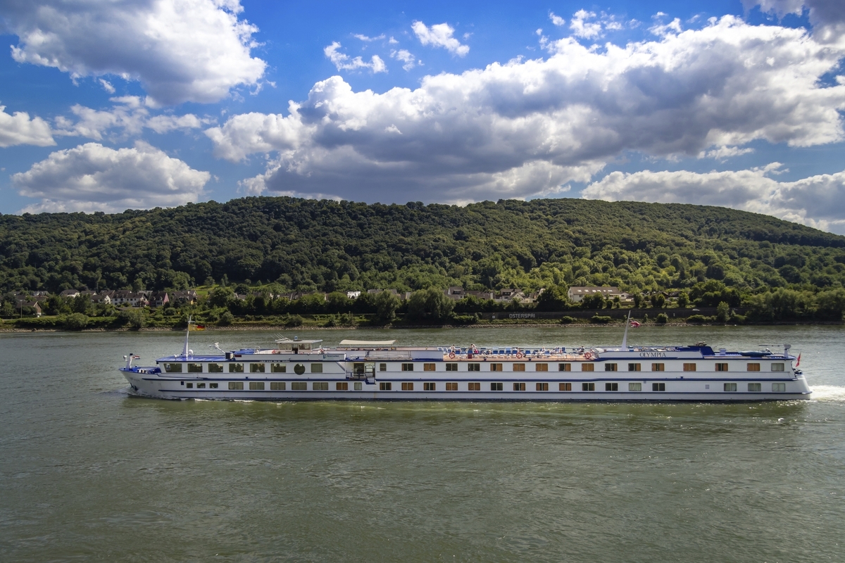 Ein Flusskreuzfahrtschiff auf einem Fluss vor einem bewaldeten Hügel.