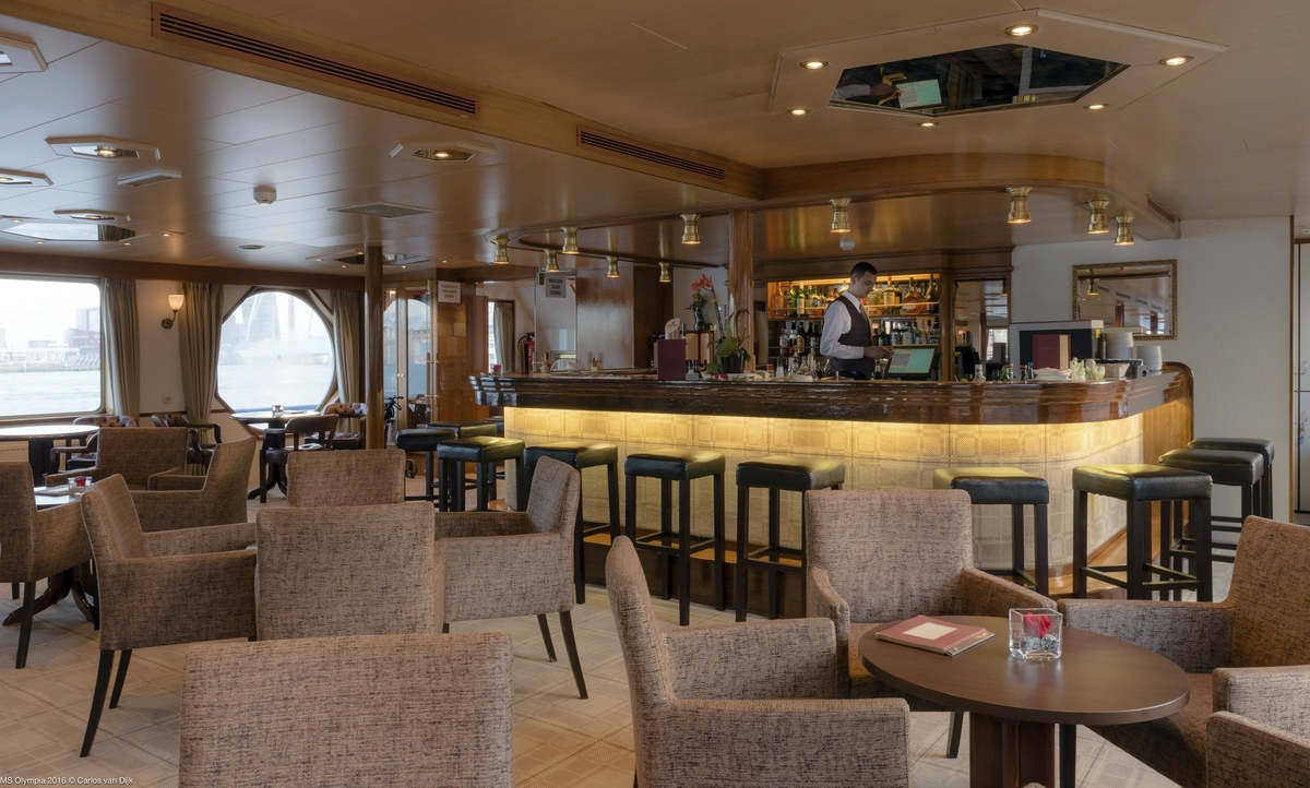 Ein Salon auf einem Schiff mit einer Bar und gemütlichen Sitzgelegenheiten.