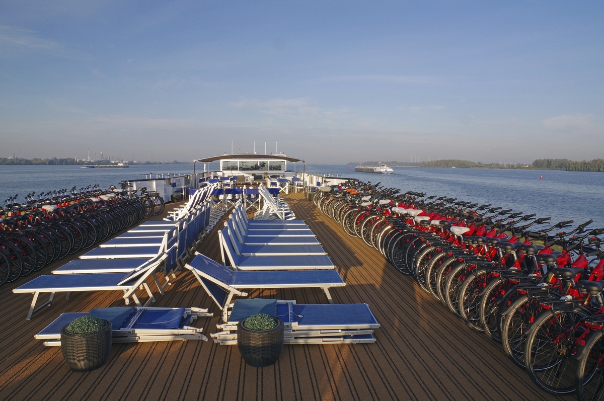 Deck eines Schiffes mit Fahrrädern und Liegestühlen am Meer bei klarem Himmel.