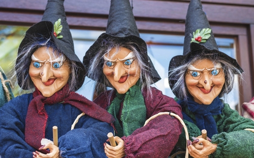 Drei Hexenpuppen mit spitzen Hüten und Besen stehen dekorativ nebeneinander.