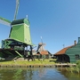 Grüne Windmühle an einem Flussufer bei sonnigem Wetter.