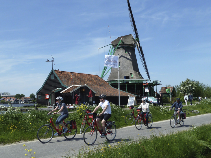 Radfahrer auf einem Weg neben einer Windmühle in Nordholland bei sonnigem Wetter