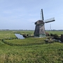 Windmühle in nordholländischer Landschaft mit Kanal und Gebäuden im Hintergrund.