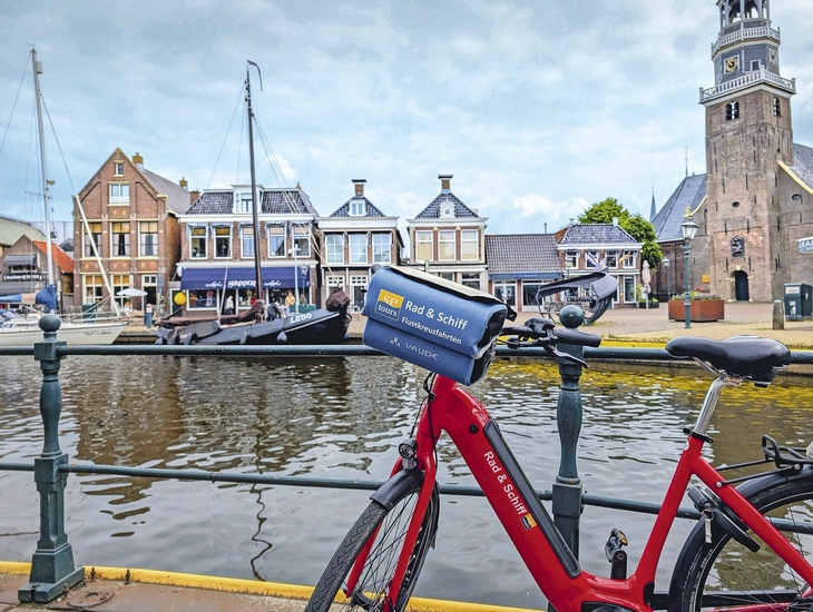 Rotes Fahrrad vor Kanal, historische Gebäude und Kirchturm im Hintergrund.