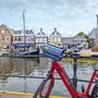 Rotes Fahrrad vor Kanal, historische Gebäude und Kirchturm im Hintergrund.