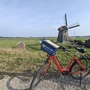 Rotes Fahrrad vor einer Windmühle in einer weiten, grünen Landschaft.