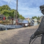 Statue eines Mannes am Kai, Boote auf Wasserweg, Bäume und Gebäude im Hintergrund