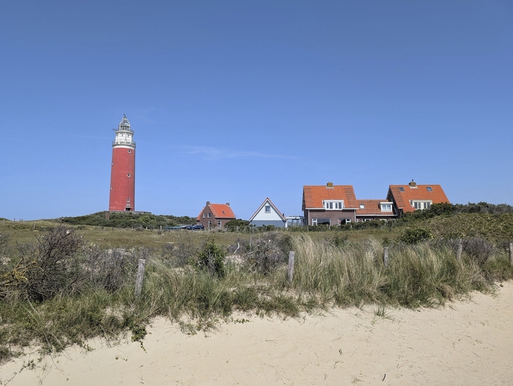 Leuchtturm auf Texel mit roten Dächern und Dünen im Vordergrund.