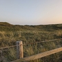 Dünenlandschaft auf Texel mit Gras und Holzzaun im Vordergrund bei Sonnenuntergang.