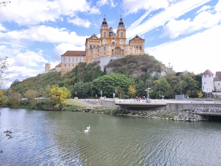 Stift Melk auf einem Hügel mit Donau im Vordergrund bei sonnigem Wetter.