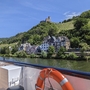 Schiff auf Fluss, Burgruine auf Hügel hinter Fachwerkhäusern, bewaldete Hänge im Hintergrund.