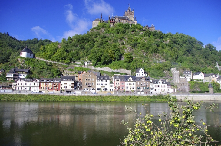 Blick auf die Reichsburg Cochem und den Fluss Mosel, umgeben von grüner Landschaft.