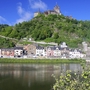 Blick auf die Reichsburg Cochem und den Fluss Mosel, umgeben von grüner Landschaft.